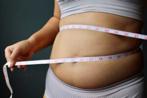 Person measuring waist representing ideal liposuction candidates and body contouring goals.