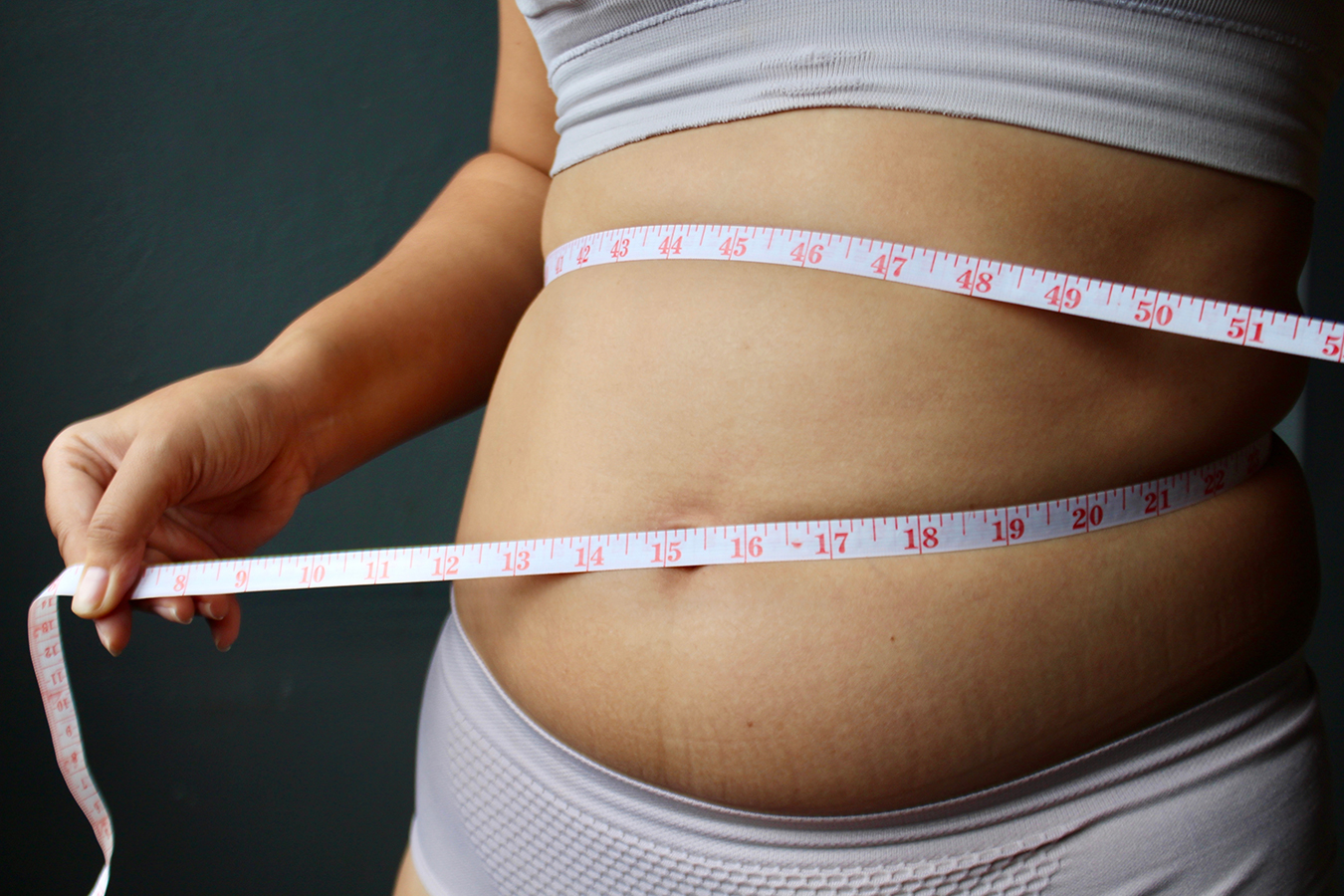 Person measuring waist representing ideal liposuction candidates and body contouring goals.
