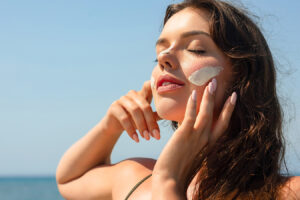 Woman applying sunscreen outdoors representing treatment for summer sun damage and facial skin repair.