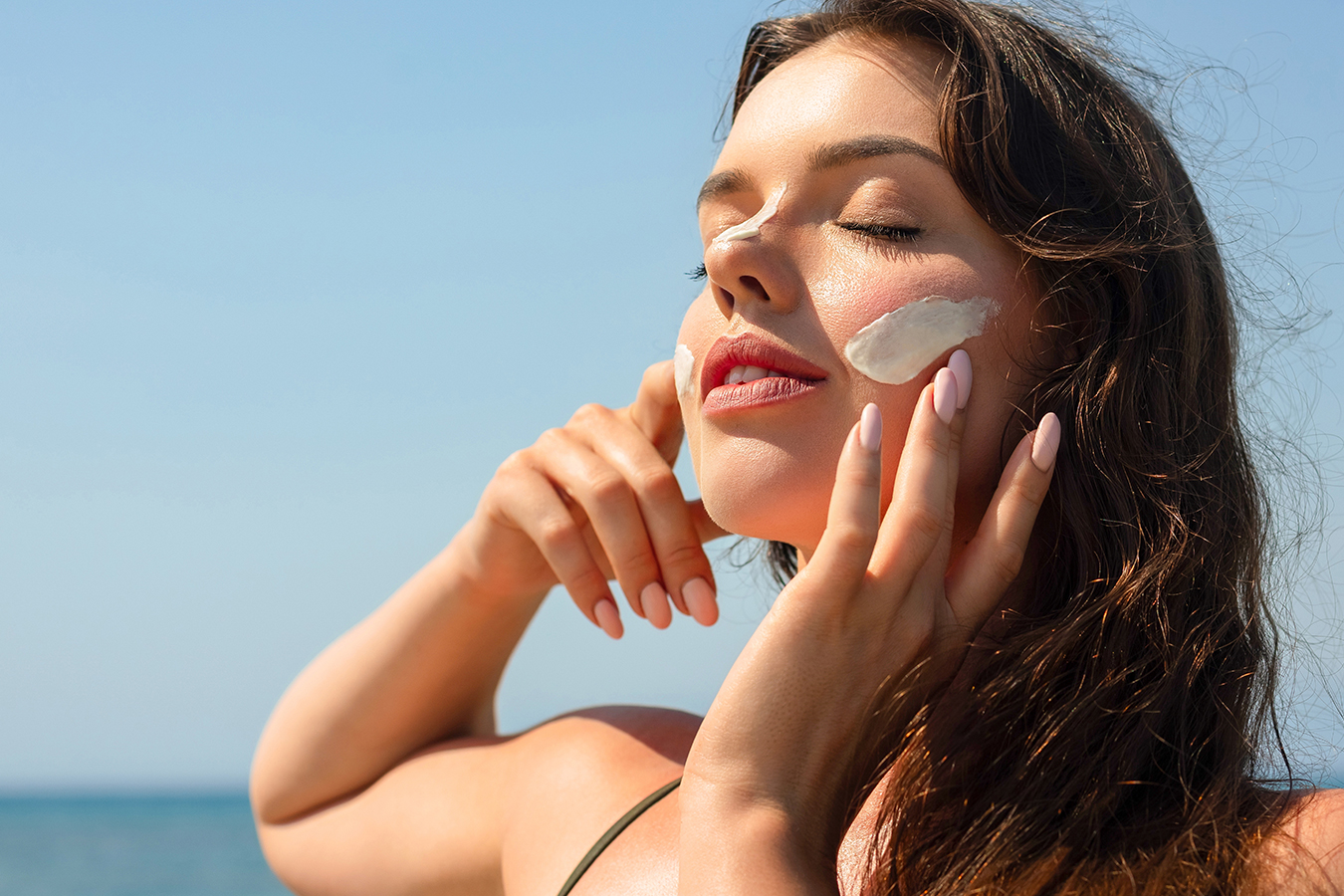 Woman applying sunscreen outdoors representing treatment for summer sun damage and facial skin repair.