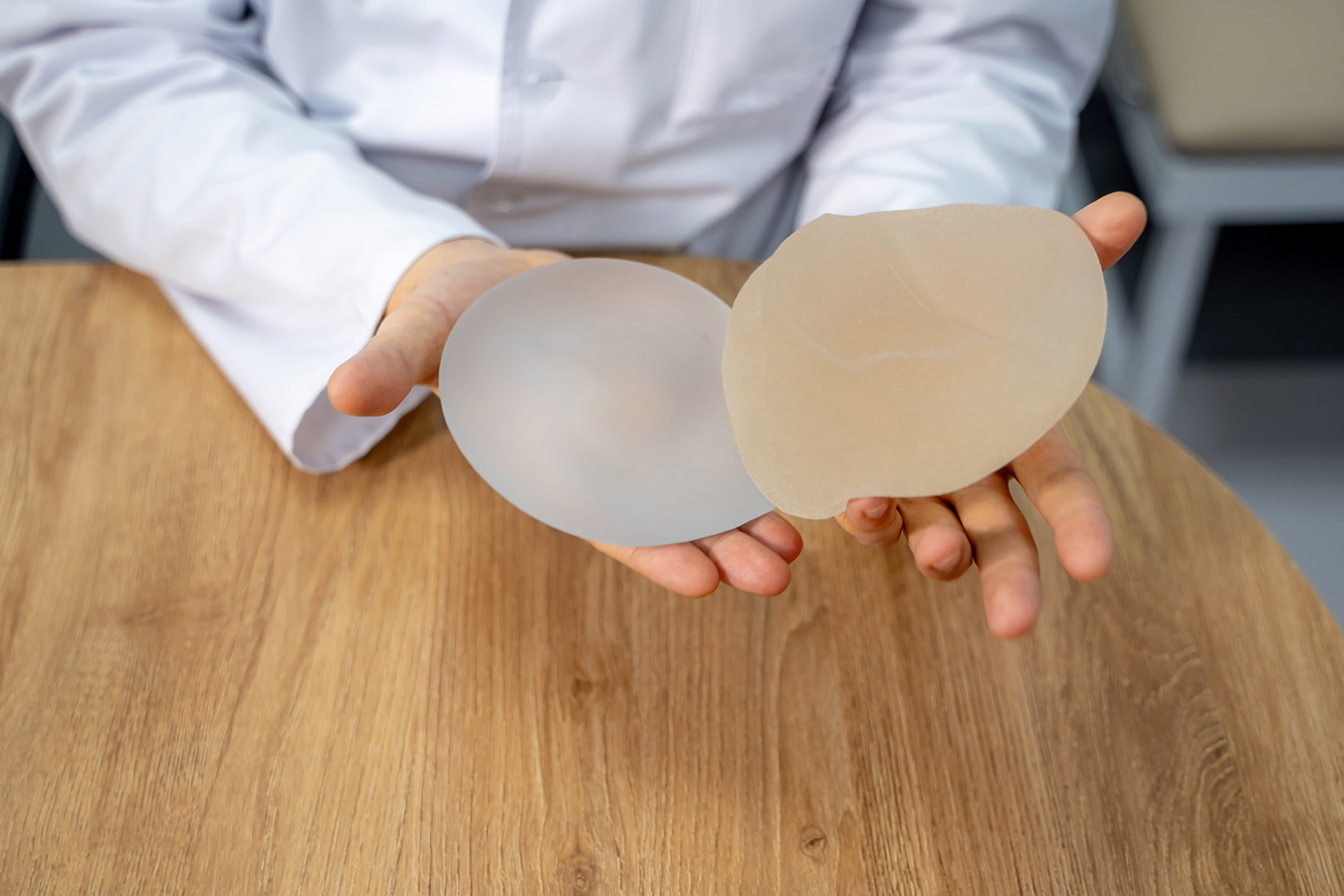Doctor holding breast implants representing implant replacement consultation and breast revision planning.