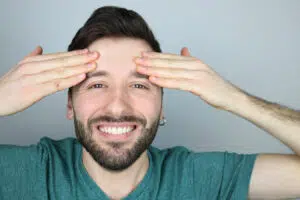 Smiling man touching forehead representing Bro-Tox treatments for men’s wrinkles and aging well.