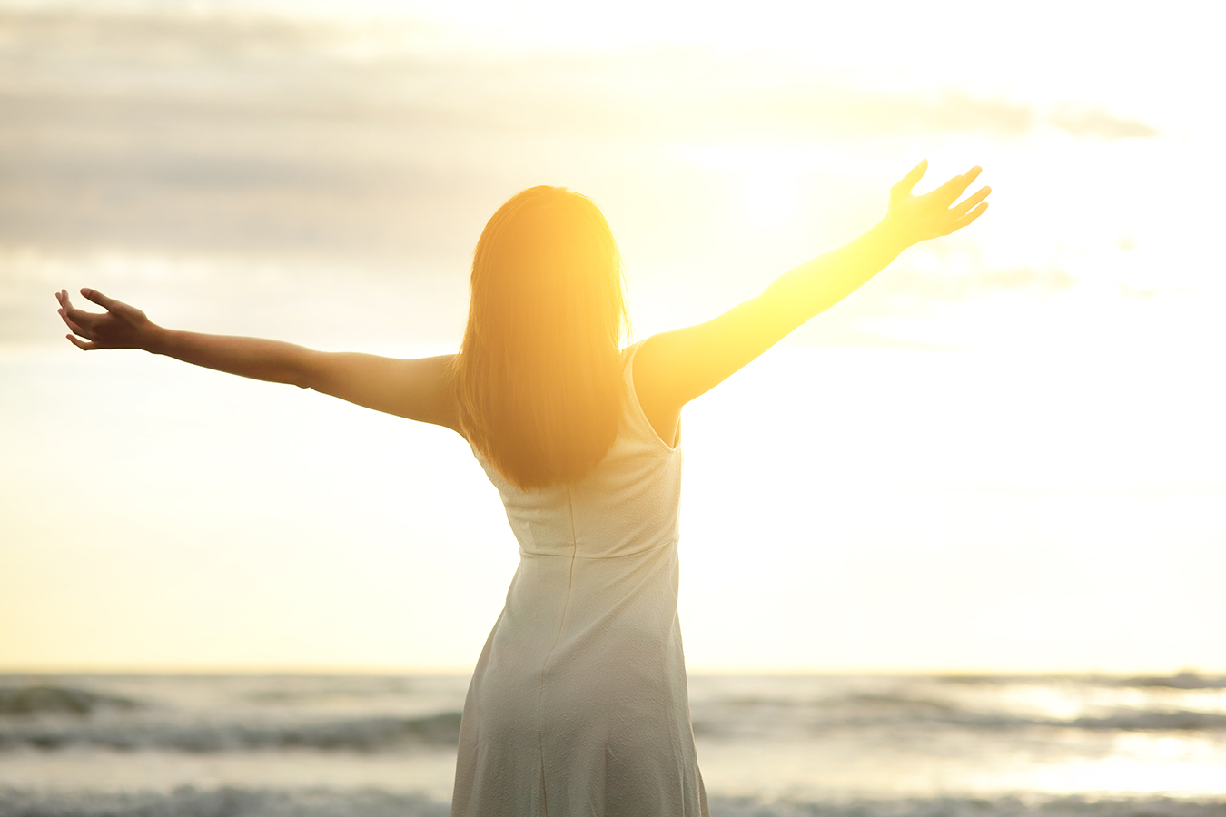 Woman facing summer sun with arms raised representing pre-summer skincare and sun protection tips.