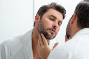 Man checking chin area in mirror for Kybella chin fat treatment information