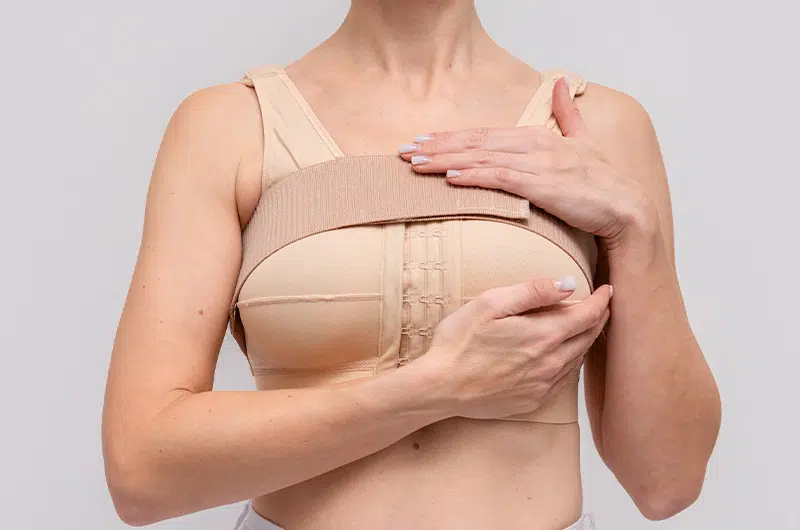 Woman wearing post-surgical compression bra and support strap after breast lift with implant procedure.