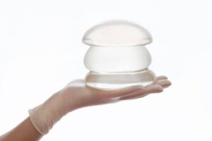 Gloved hand holding silicone breast implants, representing reasons and timing for breast implant exchange surgery.