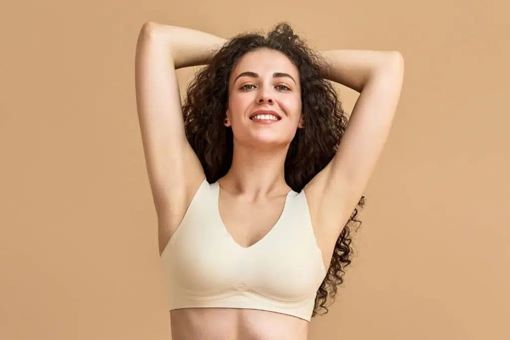 Smiling woman with natural-looking breasts wearing a neutral bra, representing ballerina yoga breast aesthetic trend
