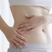 Woman holding her abdomen while considering the emotional side of tummy tuck surgery and recovery.