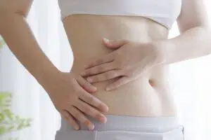 Woman holding her abdomen while considering the emotional side of tummy tuck surgery and recovery.