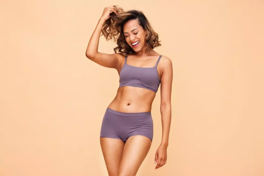 Smiling woman in purple activewear showcasing body contours, illustrating Mommy Makeover benefits and results.